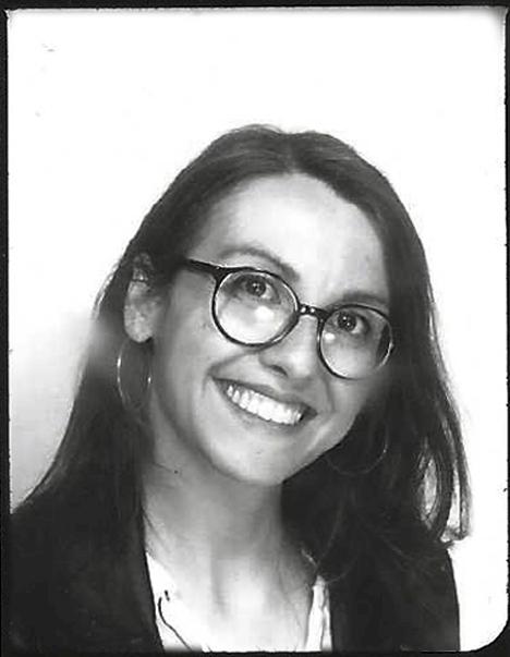 Shown is a portrait photo of Sandra Vacca in black and white. She wears her hair loose and smiles.